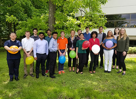 Group of people standing outside smiling while holding different color balloons