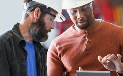 Two men with hardhats looking at a tablet